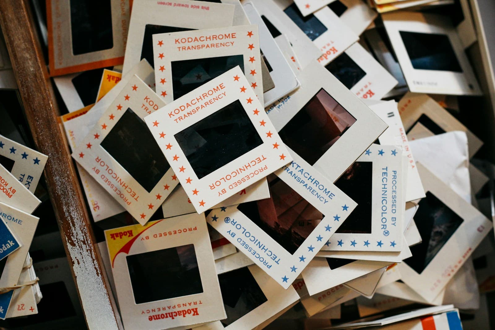 A pile of Kodachrome and Ektachrome transparencies in Technicolor cardboard mounts spilling out of a wooden box