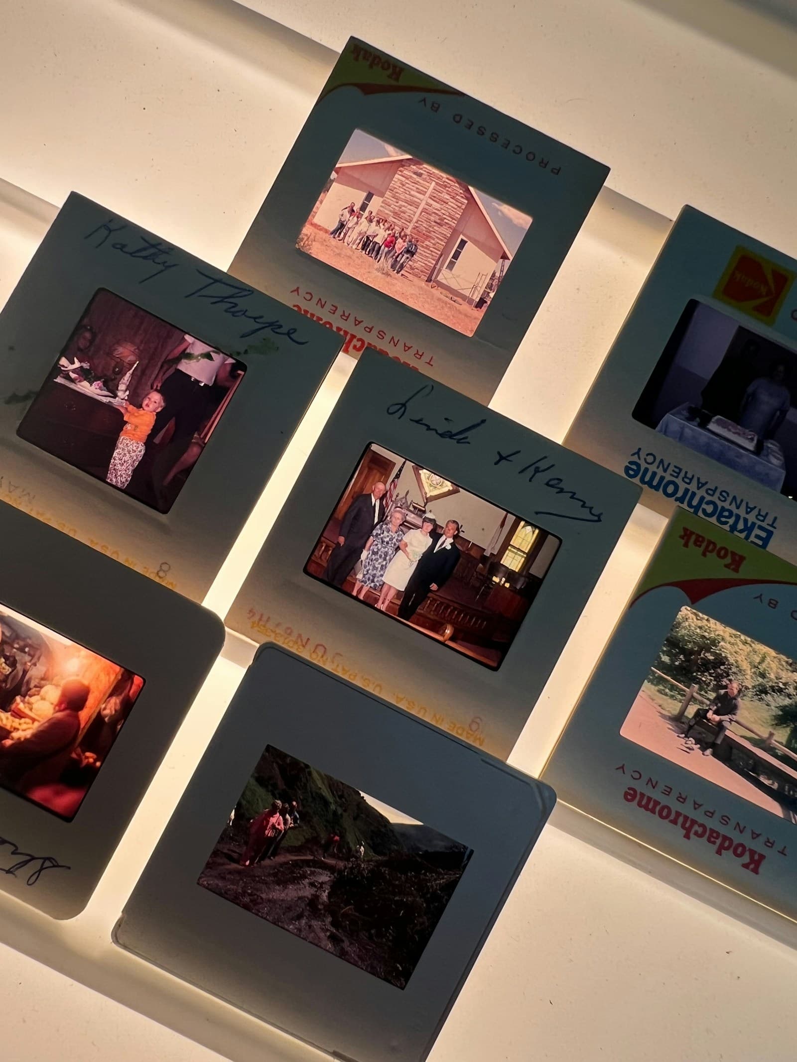 Vintage Kodachrome and Ektachrome slides in cardboard mounts with handwritten labels, glowing on a light table in a dim room