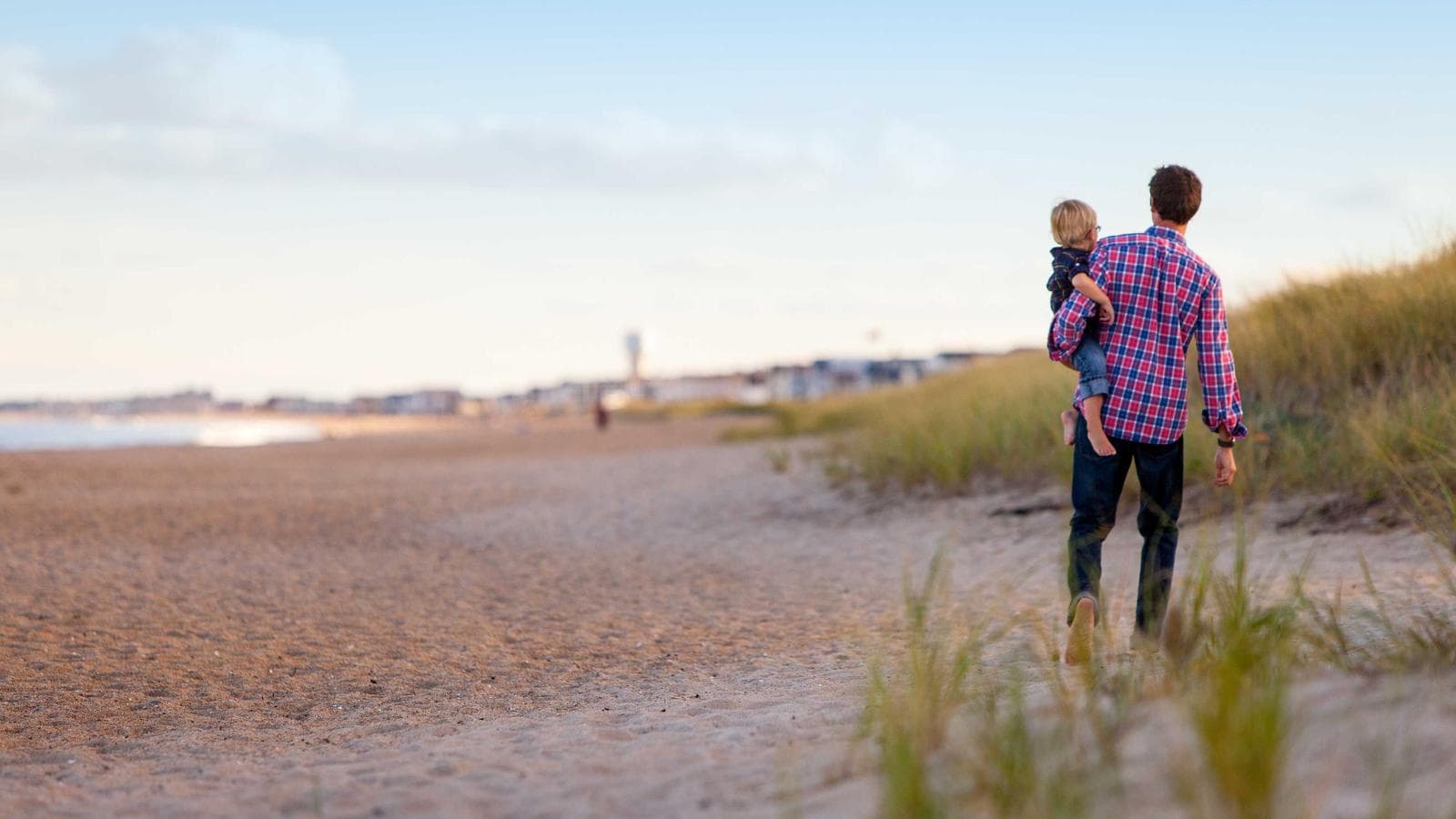 Father carrying a child along a sandy beach
